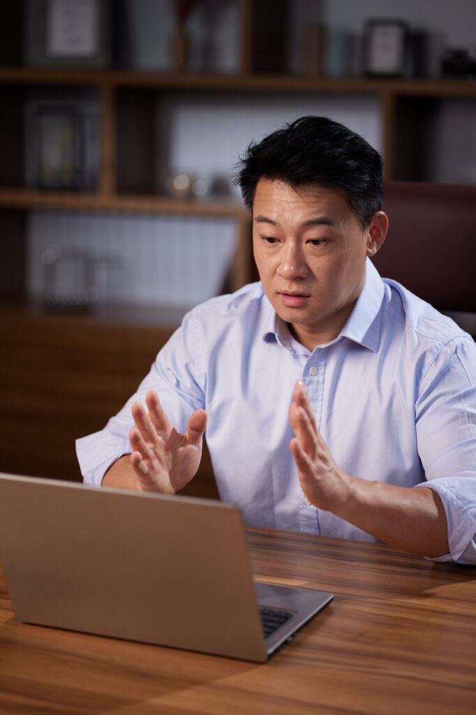 Asian man holding online webinar using laptop webcam, sitting in a home office. Man having online